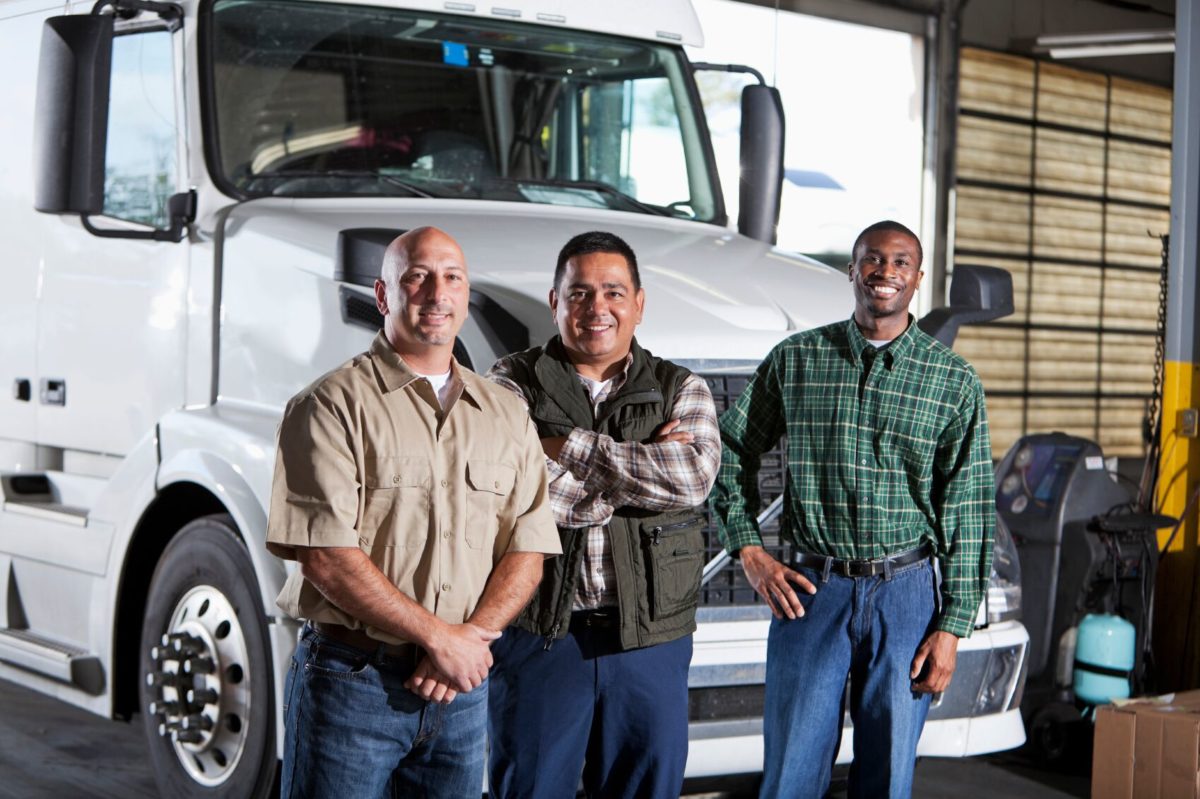 Pictured is three truck drivers in front of a semi truck.