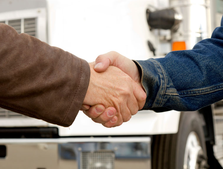 Two men shaking hands in front of a white semi