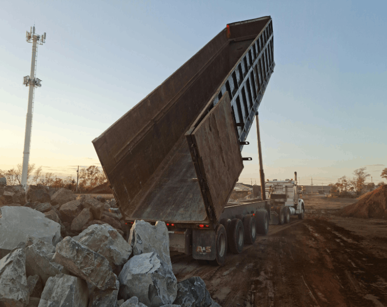 Dump trucking dumping boulders into a pile in construction site