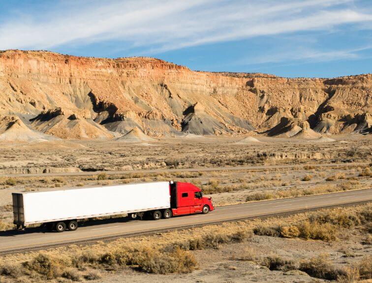 Image of red and white semi truck driving on a mountainous highway