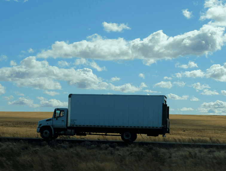 Side view of semi truck driving on road, corn fields in back
