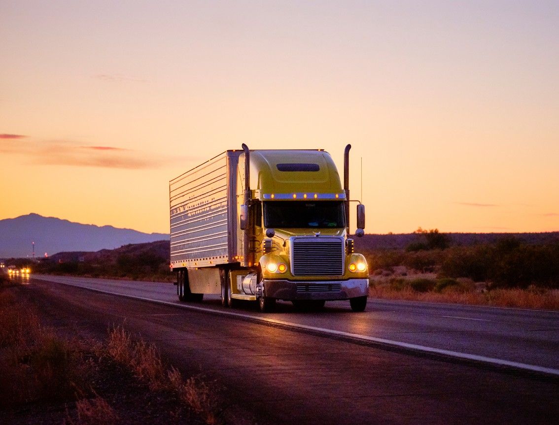 Yellow semi truck driving down an empty highway with a sunset
